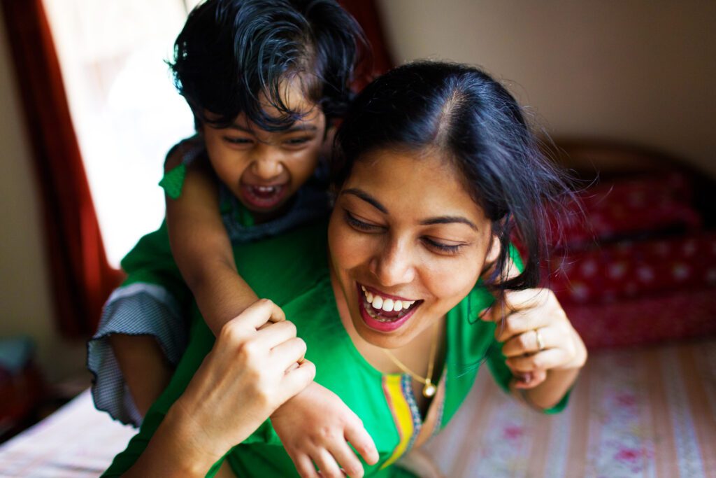 smiling South Asian woman giving her toddler a piggy-back ride